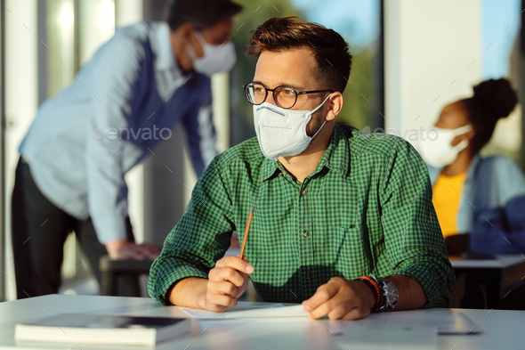 College student with face mask thinking while having an exam in the classroom.