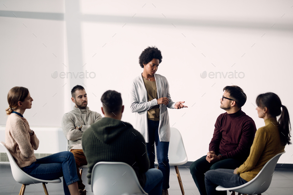 African American woman standing while talking during group therapy meeting.