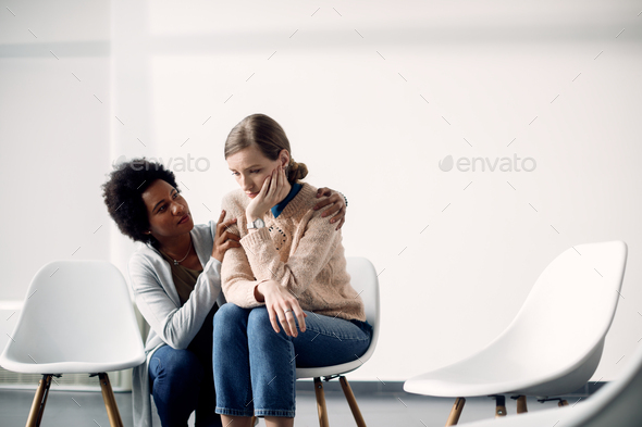 Caring African American woman consoling sad woman before group therapy meeting. - Stock Photo - Images