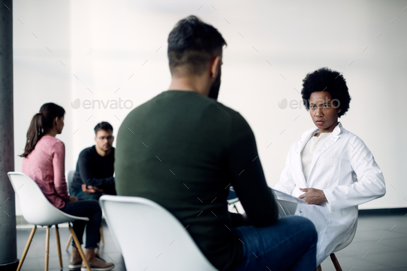 African American psychotherapist talking to male patient during group therapy.