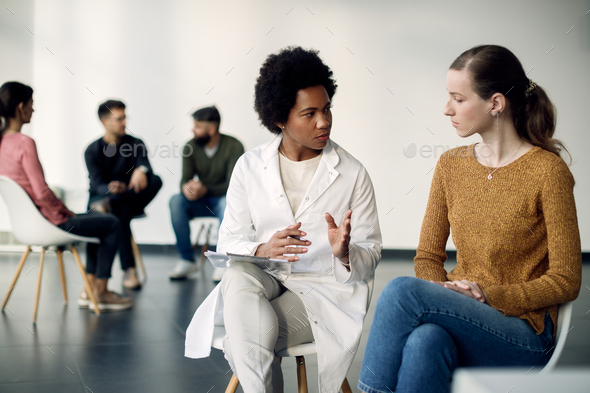 Black female mental health professional talking to female patient during group therapy.