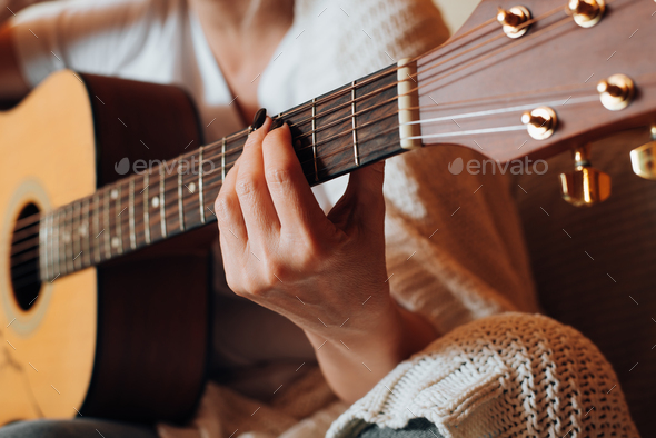 Musical hobby, learn music concept. Close-up of woman playing an acoustic guitar, indoors.