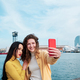 Two women taking selfies with a mobile phone outdoors on the sea promenade. - PhotoDune Item for Sale