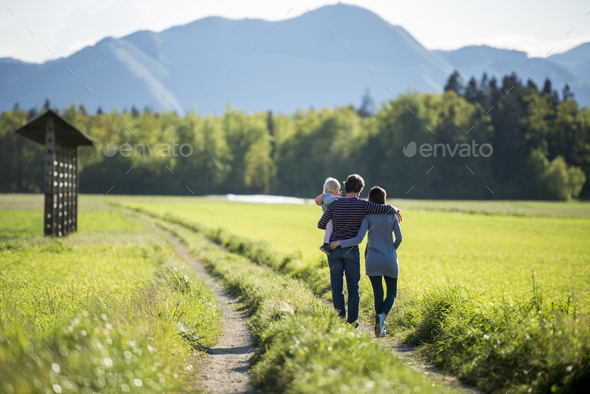 Young family - husband holding a toddler and hugging his wife - standing on a country road - Stock Photo - Images