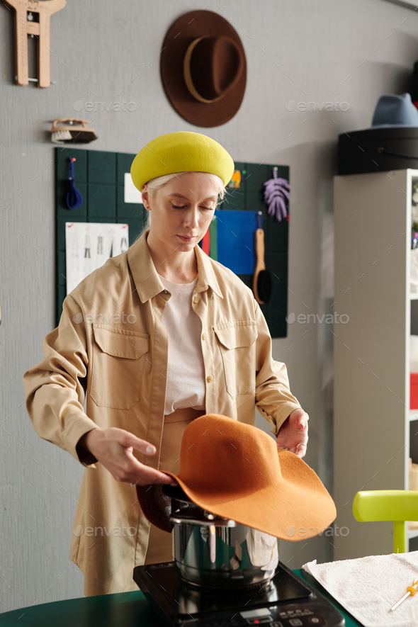 Young creative hat maker steaming new item over pan with boiling water  Stock Photo by Pressmaster