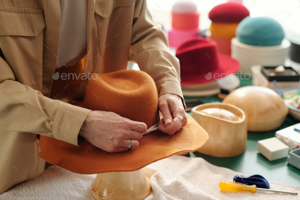 Close-up of young creative craftswoman fixing decorative shoelace arount hat - Stock Photo - Images