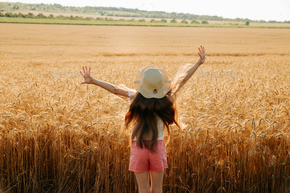rear view of little kid girl with hat raise your hands up in wheat land