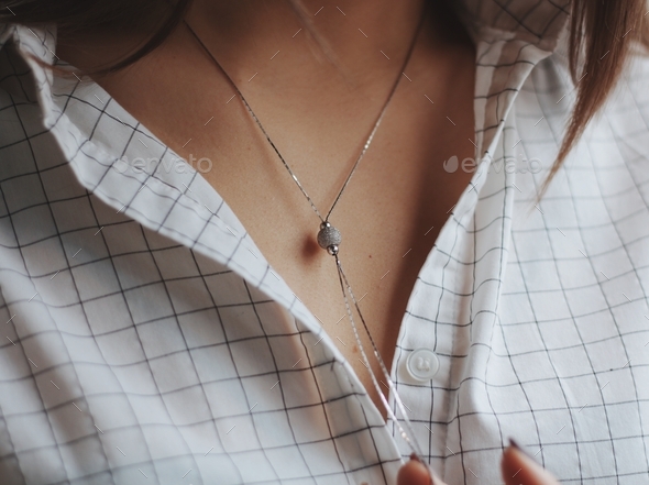Closeup shot of a female wearing a white shirt and a delicate silver charm necklace
