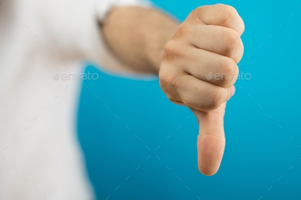 Closeup of a person doing the thumbs-down gesture under the lights against a blue background