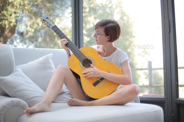 Lady with short black hair and glasses playing the guitar on the couch