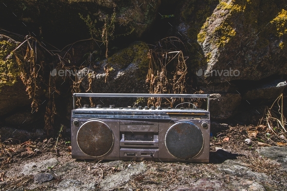 Retro outdated portable stereo boombox radio cassette recorder on the ground around mossy stones