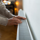 Closeup of woman in sweater puts hands on room central heating battery to warm up in cold apartment - PhotoDune Item for Sale