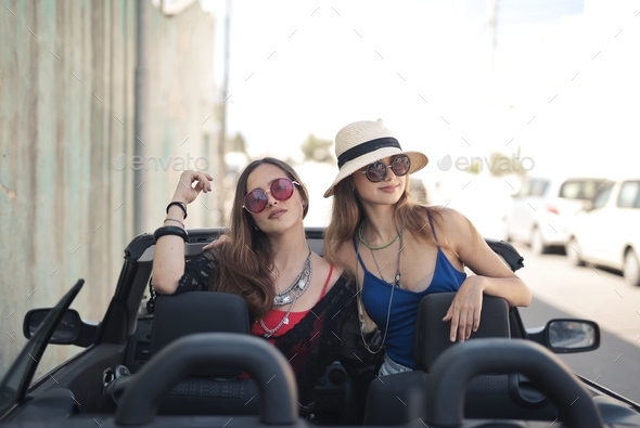 Beautiful shot of two female friends with accessories on a convertible sports car - Stock Photo - Images