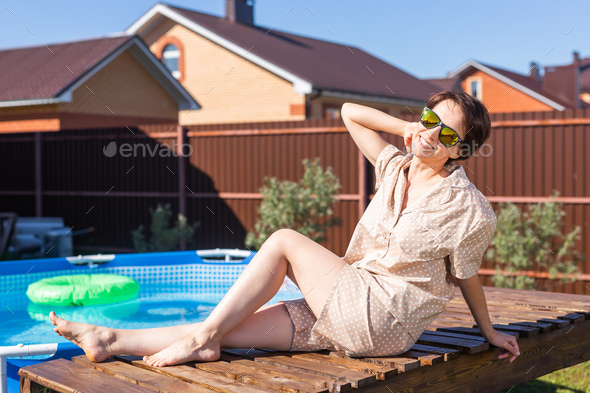 Portrait of pretty young woman in pajama sitting near inflatable swimming pool - summer and country - Stock Photo - Images