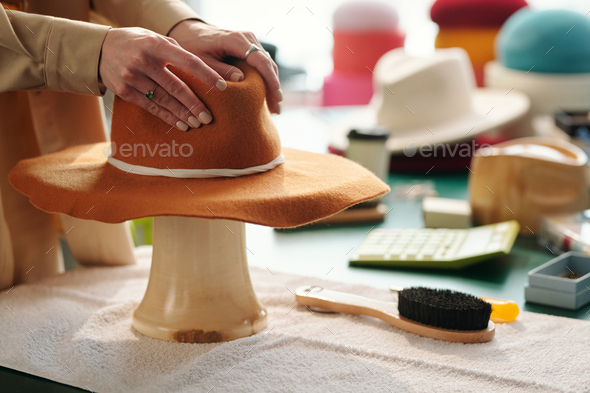 Hands of young craftswoman forming shape of brown felt hat - Stock Photo - Images