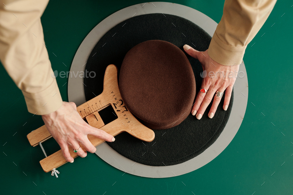 Above angle of pork pie hat and hands of craftswoman with wooden tool - Stock Photo - Images