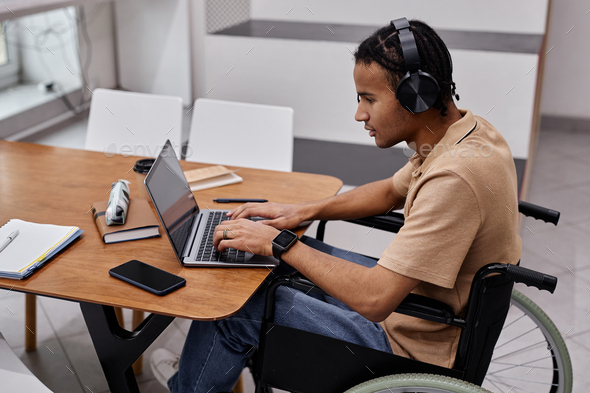Black young man with disability using laptop in college - Stock Photo - Images