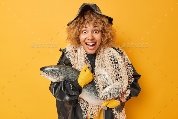 Cheerful impressed female fisher carries salmon fishing net around neck stares wondered cannot belie