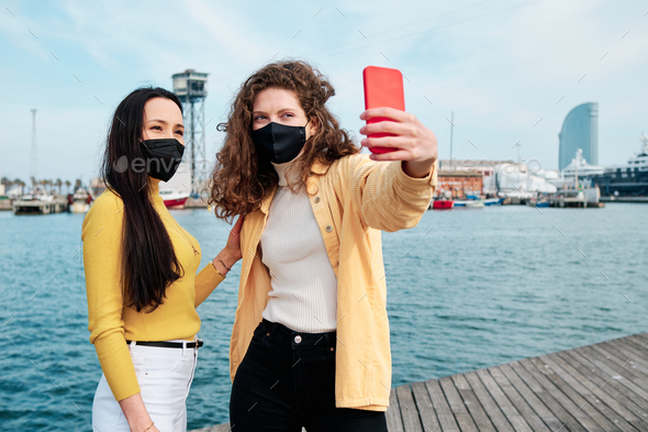 Young women with face mask taking selfies with a mobile phone outdoors. - Stock Photo - Images