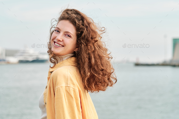 Woman looking at the camera and smiling while posing near the water outdoors. - Stock Photo - Images