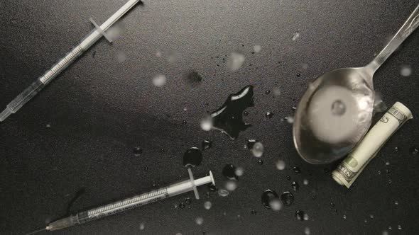 Spoon with heroin falls on a black table with syringes