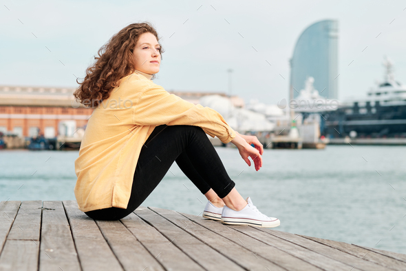Relaxed woman looking away while sitting on promenade. - Stock Photo - Images