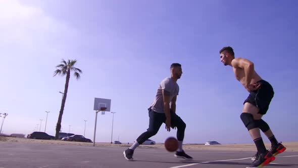 A man takes a layup shot while playing one-on-one basketball hoops on a beach court alt