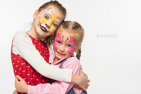 cute children with cat muzzle and butterfly paintings on faces embracing while looking at camera