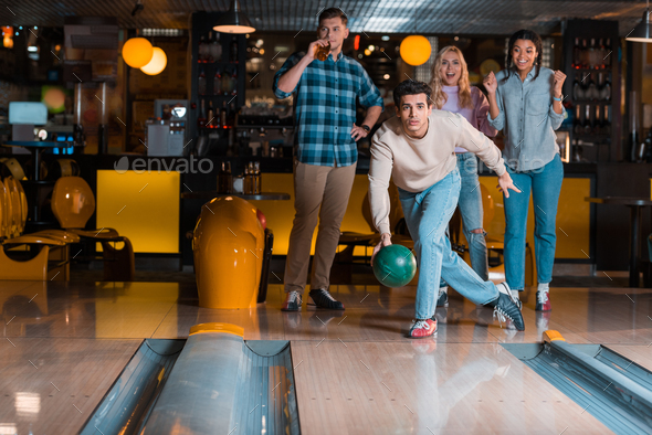 handsome young man throwing bowling ball on skittle alley near ...