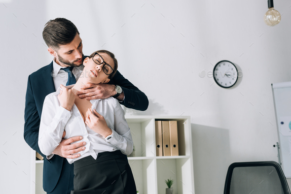 handsome businessman hugging sexy secretary with closed eyes in office