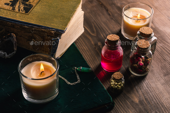 Jars with magic herbs and tincture, books and candles on wooden background