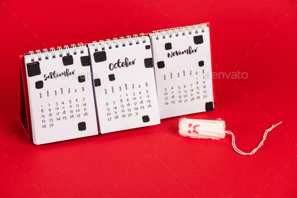 Calendar and hygienic tampon with sad face expression on red background