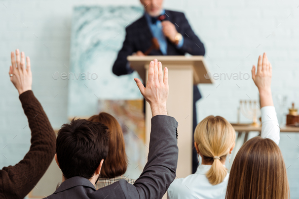 back view of buyers raising hands to auctioneer during auction - Stock Photo - Images