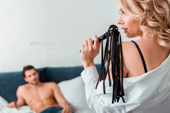 selective focus of attractive woman holding flogging whip near muscular man  on bed Stock Photo by LightFieldStudios