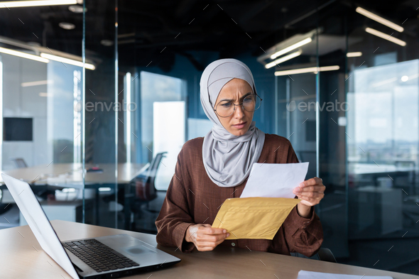 Upset business woman in hijab working inside office, woman received letter envelope mail with bad - Stock Photo - Images