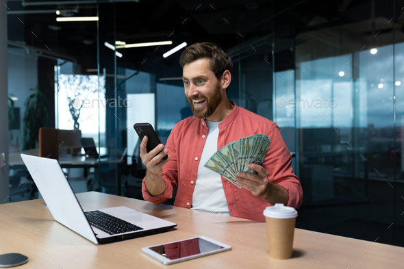 Successful businessman in red shirt celebrating victory and good achievement holding phone and - Stock Photo - Images