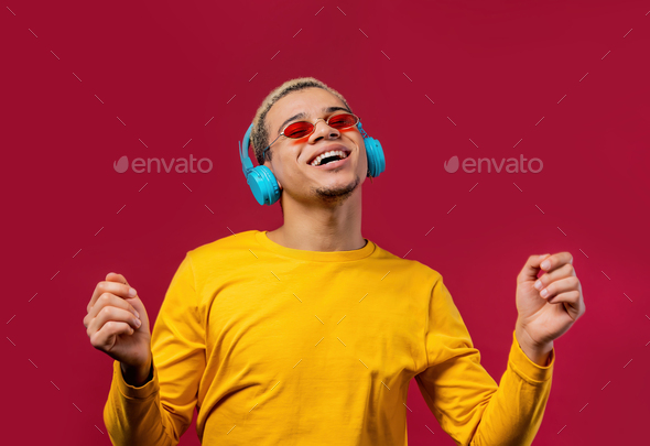 Positive man listening music, enjoying dance with headphones on red studio background.  - Stock Photo - Images