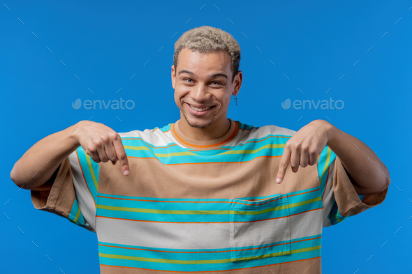 Happy man pointing down to advertising area. Blue background. Young guy asking click subscribe below