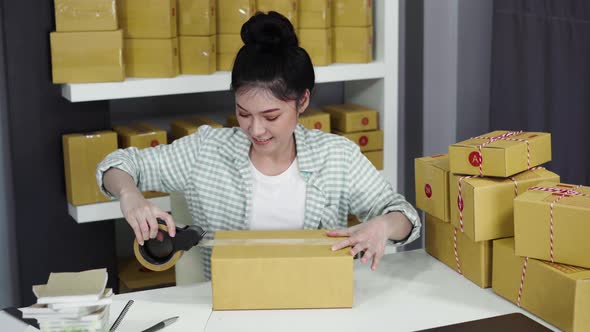woman online entrepreneur using tape to packing parcel box at home office, prepare product