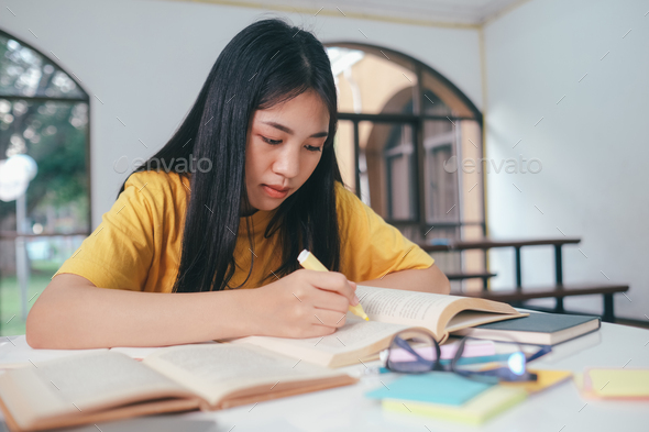 Serious Asian female student reading books for exam preparation - Stock Photo - Images