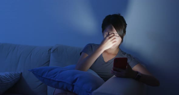 Woman use of mobile phone at night and sit on sofa at home alt