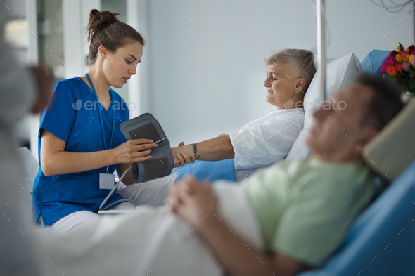 Young nurse chcecking blood presure to senior patient. - Stock Photo - Images
