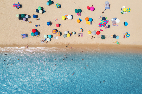 Aerial view of umbrellas on sandy beach, people in blue sea - Stock Photo - Images