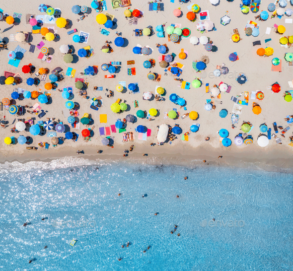 Aerial view of umbrellas on sandy beach, people in blue sea - Stock Photo - Images
