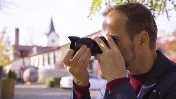 A Middleaged Handsome Caucasian Man Takes Pictures with a Camera As He Sits on a Bench