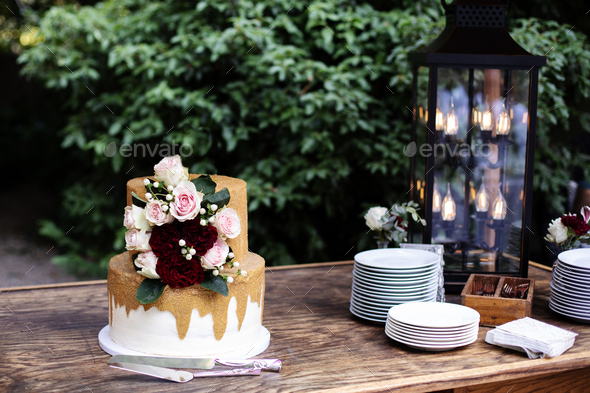 Two tiered white and gold wedding cake with red and pink roses and ruscus leaves