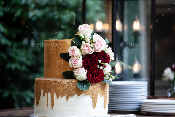 Two tiered white and gold wedding cakek roses and ruscus leaves on a wooden vintage cart