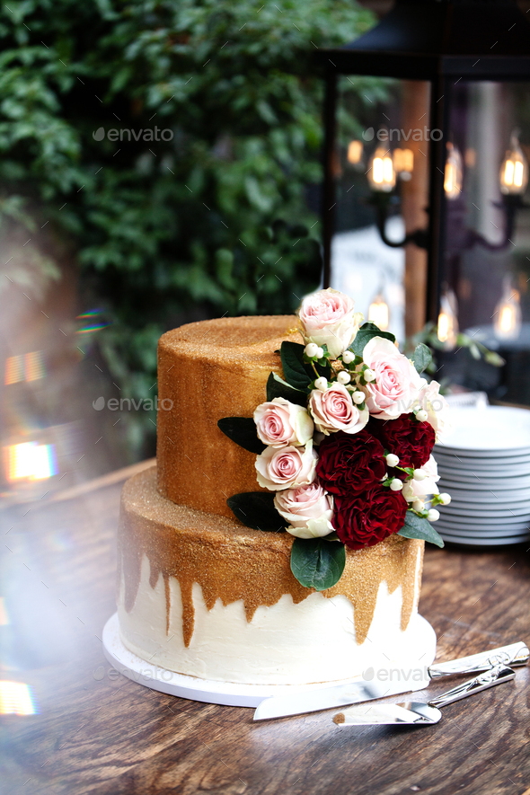 white and gold wedding cake with red and pink roses and ruscus leaves on a wooden vintage cart