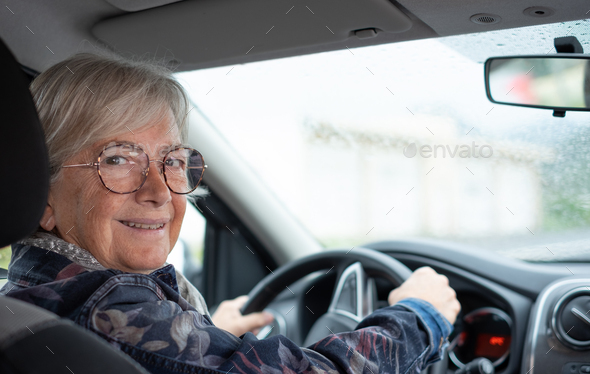 Senior woman driver driving her car on a rainy day. Elderly woman holding the steering wheel