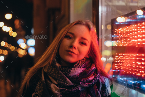 young beautiful woman in glasses on a city street at night in the light of shop windows